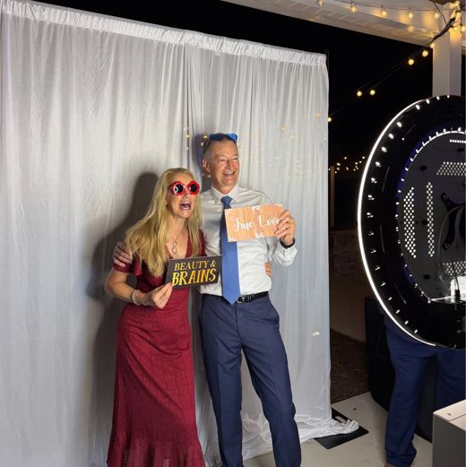 Wedding guests posing with props by the ring-light photo booth and a white draped backdrop